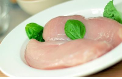 Two raw chicken breasts on a white oval dish with basil leaves.